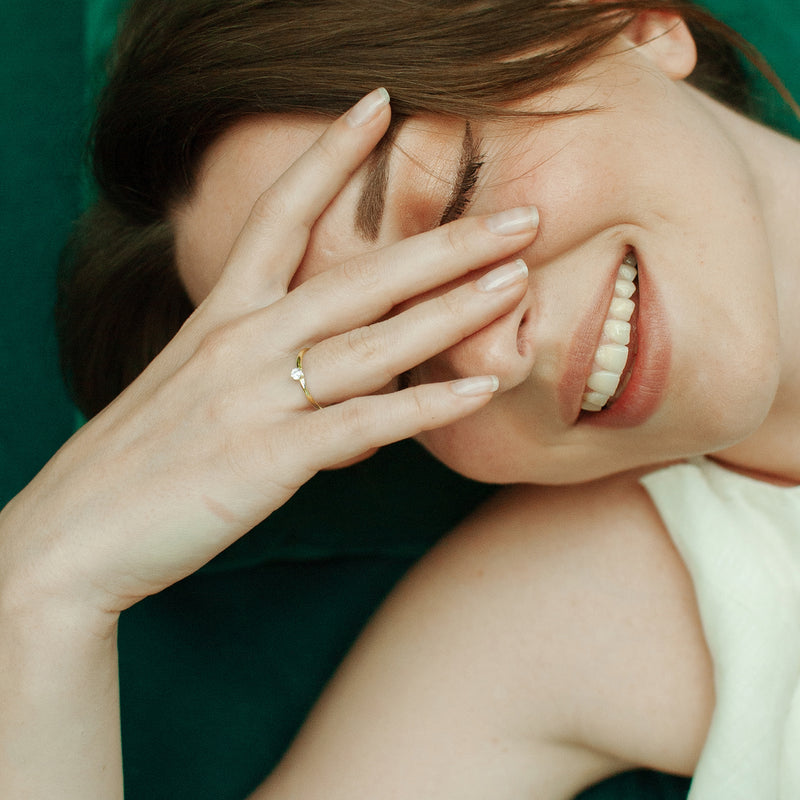 Eine lächelnde Frau trägt einen feinen Goldring mit funkelndem Zirkonia an der Hand – emotionales Schmuckfoto im edlen Amoonic Stil.